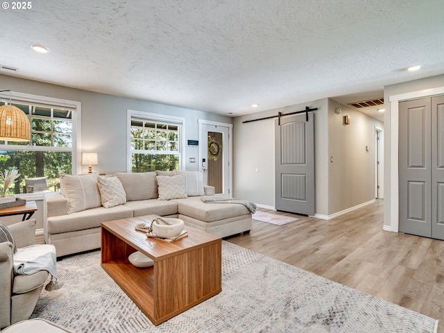 living room with a barn door, visible vents, a textured ceiling, and light wood-style flooring