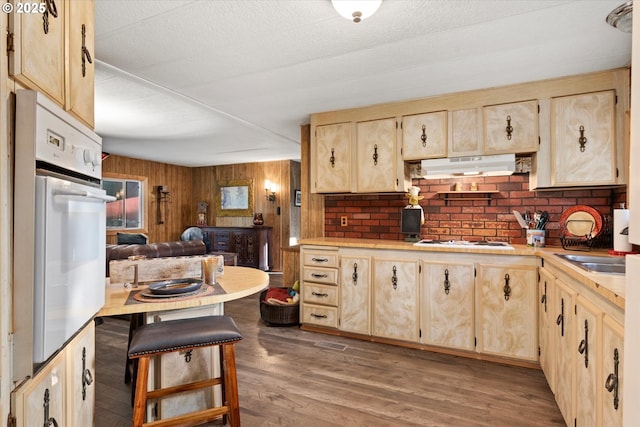 74576 Thompson Rd, Elgin, OR 97827 - kitchen featuring under cabinet range hood, light brown cabinets, white appliances, wood finished floors, and wood walls