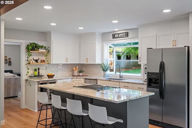kitchen with a breakfast bar area, open shelves, a sink, stainless steel fridge with ice dispenser, and white cabinets