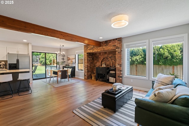 living area featuring light wood-type flooring, a textured ceiling, beamed ceiling, and an inviting chandelier