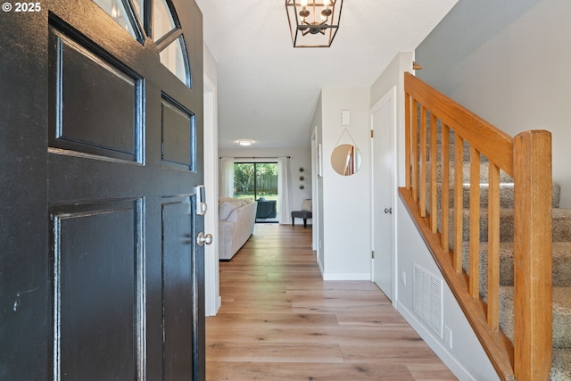 entrance foyer with a notable chandelier, light wood-style floors, stairs, baseboards, and visible vents