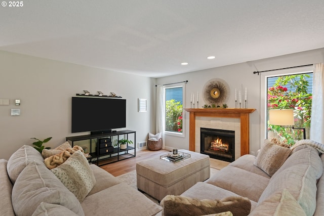 living room featuring visible vents, wood finished floors, baseboards, recessed lighting, and a tiled fireplace