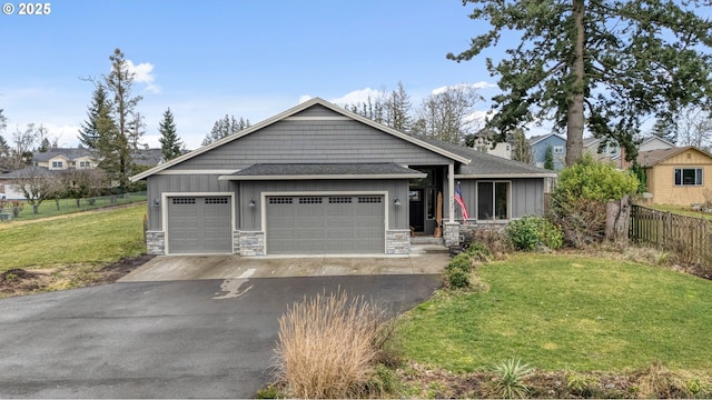 craftsman house with an attached garage, fence, stone siding, a front lawn, and board and batten siding