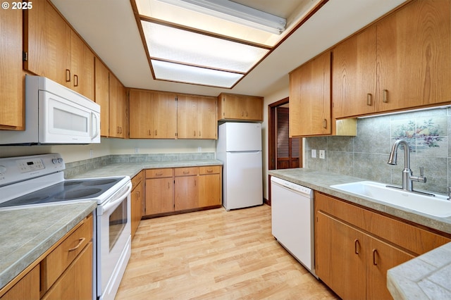 kitchen featuring light wood-style flooring, white appliances, a sink, decorative backsplash, and light countertops