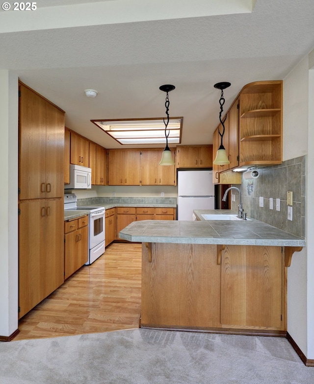 kitchen with a peninsula, a breakfast bar, a sink, white appliances, and light colored carpet