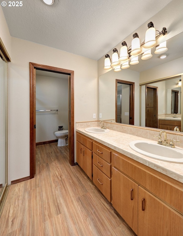 bathroom with double vanity, toilet, wood finished floors, and a sink
