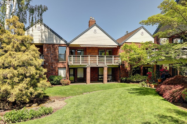 rear view of house with brick siding, a chimney, a lawn, and a balcony