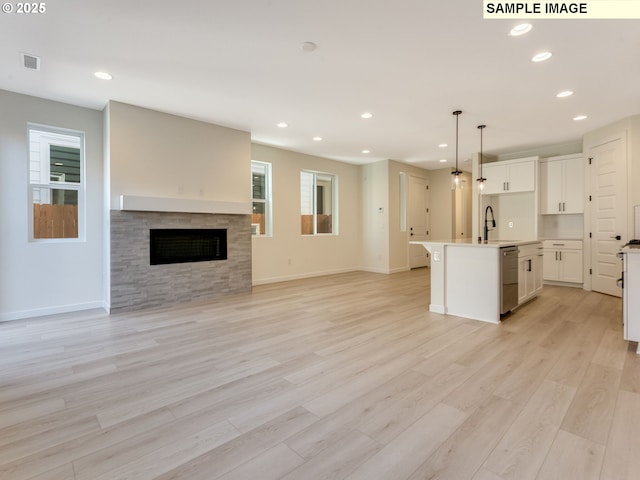 kitchen with light wood finished floors, dishwasher, a fireplace, white cabinetry, and a sink