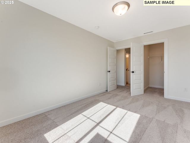 unfurnished bedroom with baseboards, a walk in closet, visible vents, and light colored carpet