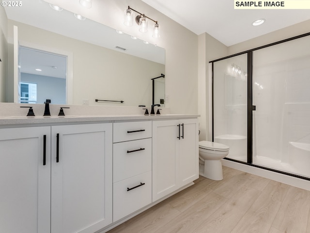 bathroom featuring double vanity, a stall shower, wood finished floors, and toilet