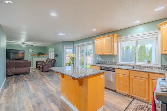 kitchen featuring a kitchen island, a kitchen breakfast bar, open floor plan, stainless steel dishwasher, and a glass covered fireplace