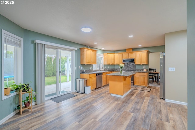 kitchen featuring stainless steel appliances, a sink, light wood-style flooring, and a center island