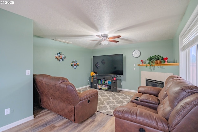 living area with light wood-type flooring, baseboards, a textured ceiling, and a tile fireplace