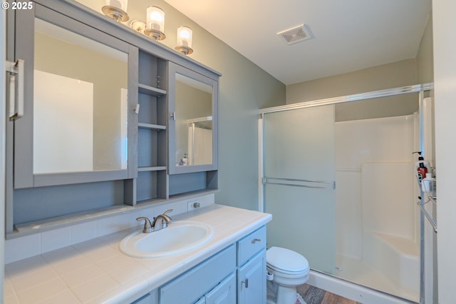 bathroom with toilet, a stall shower, vanity, and visible vents