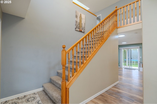 staircase featuring a high ceiling, wood finished floors, and baseboards