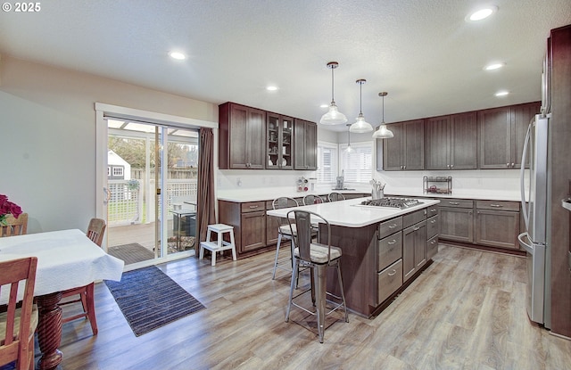 kitchen featuring a kitchen island, a breakfast bar area, hanging light fixtures, dark brown cabinetry, and light wood-type flooring