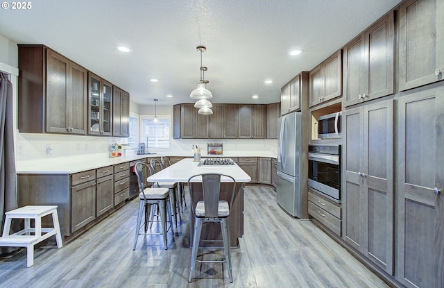 kitchen with a breakfast bar, decorative light fixtures, a center island, light wood-type flooring, and stainless steel appliances