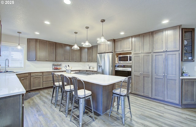 kitchen with stainless steel appliances, sink, pendant lighting, and light hardwood / wood-style flooring