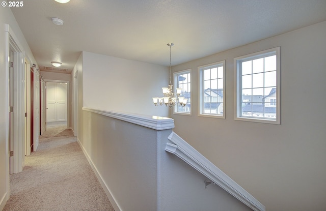 hall featuring light carpet and an inviting chandelier