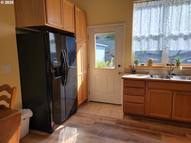 kitchen with light wood-style floors, brown cabinetry, black fridge, a sink, and light countertops