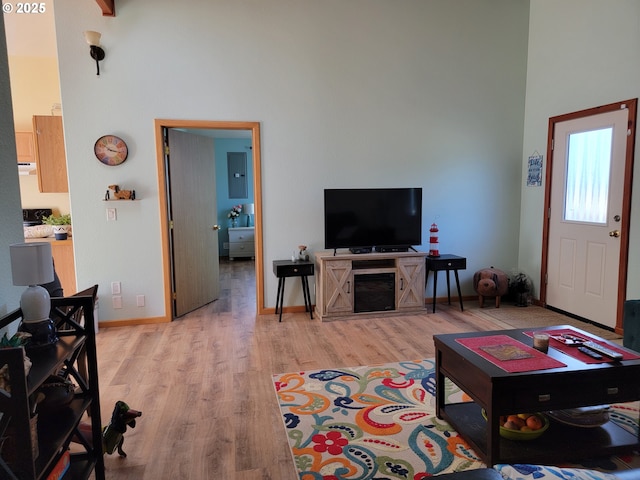 living area with electric panel, a towering ceiling, and light wood-type flooring