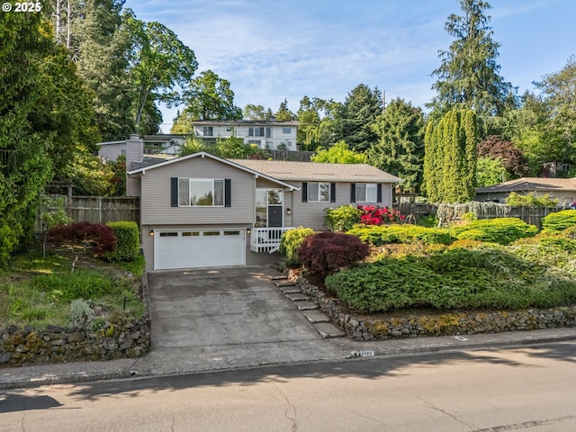 raised ranch with fence, a garage, asphalt driveway, and a chimney