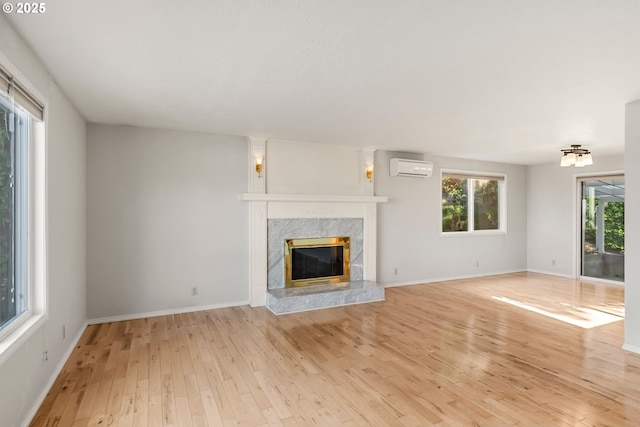 unfurnished living room featuring an AC wall unit, light wood-style flooring, a fireplace, and baseboards