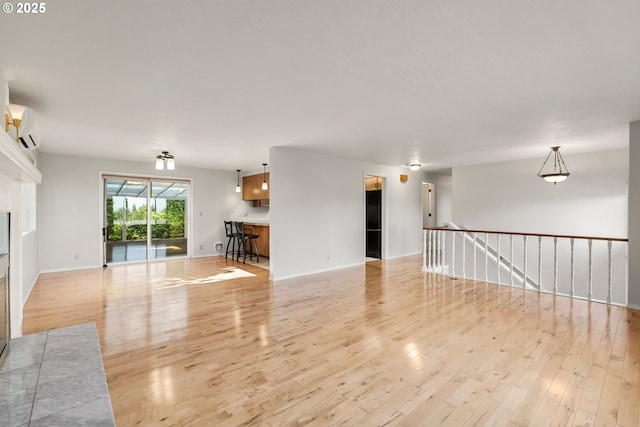 unfurnished living room featuring light wood finished floors, a wall mounted air conditioner, and baseboards