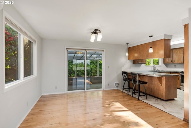 kitchen featuring brown cabinetry, light wood-type flooring, a breakfast bar area, a peninsula, and baseboards