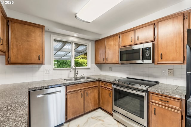 kitchen featuring stainless steel appliances, a sink, light marble finish flooring, brown cabinetry, and recessed lighting