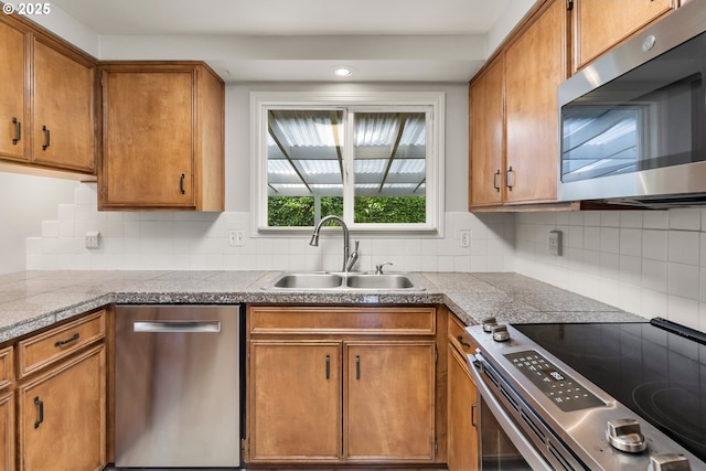 kitchen with appliances with stainless steel finishes, a sink, tile counters, brown cabinets, and decorative backsplash