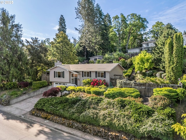 split foyer home featuring fence, a garage, driveway, and view of wooded area