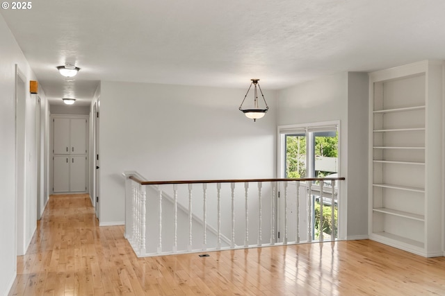 corridor featuring an upstairs landing, built in shelves, light wood-style flooring, and baseboards