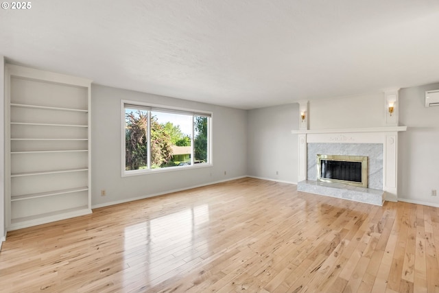 unfurnished living room with light wood-type flooring, a fireplace, an AC wall unit, and baseboards