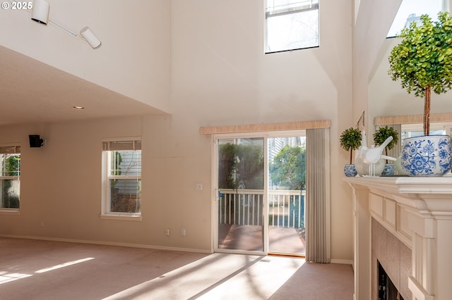 unfurnished living room with a wealth of natural light, carpet, a high ceiling, and a tiled fireplace