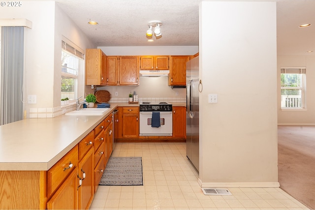 kitchen with electric range, stainless steel refrigerator, light countertops, under cabinet range hood, and a sink