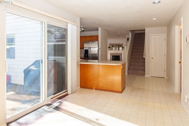 kitchen featuring a textured ceiling, a peninsula, light countertops, brown cabinets, and stainless steel fridge