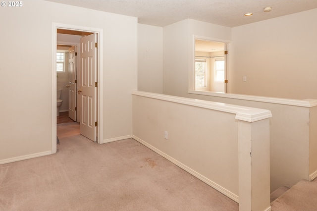 hall featuring carpet floors, plenty of natural light, a textured ceiling, and an upstairs landing