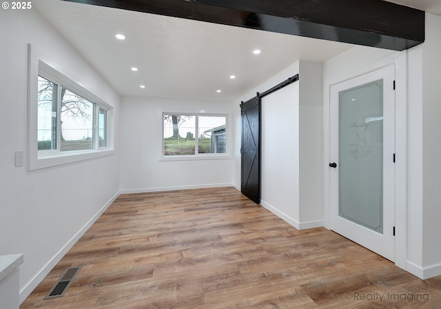 spare room featuring beamed ceiling, a barn door, a textured ceiling, and light hardwood / wood-style floors