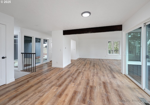 unfurnished living room with lofted ceiling with beams, a textured ceiling, and light hardwood / wood-style flooring