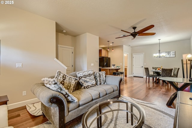 living room featuring wood-type flooring, ceiling fan with notable chandelier, and a textured ceiling