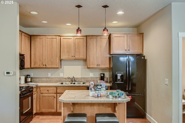 kitchen with sink, decorative light fixtures, light wood-type flooring, a kitchen island, and black appliances