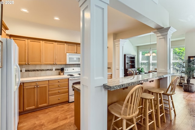 kitchen featuring white appliances, decorative columns, a breakfast bar area, light wood-style flooring, and decorative backsplash