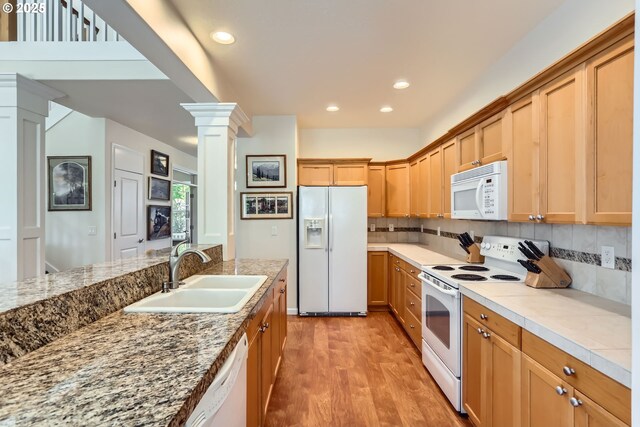 kitchen featuring white appliances, a sink, ornate columns, light wood-style flooring, and decorative backsplash