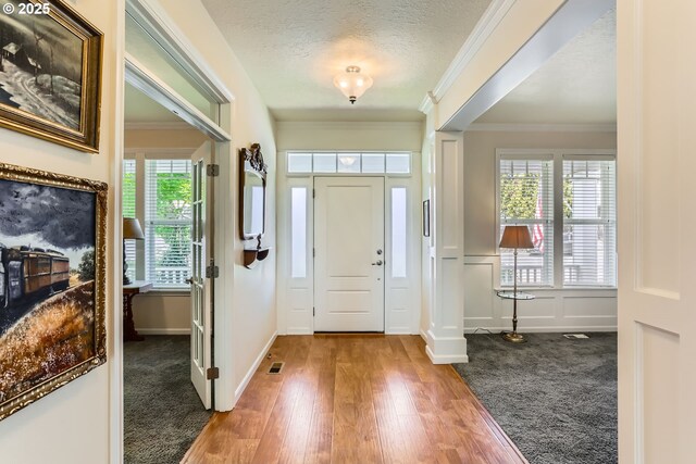 entrance foyer featuring wood finished floors, crown molding, a textured ceiling, and baseboards