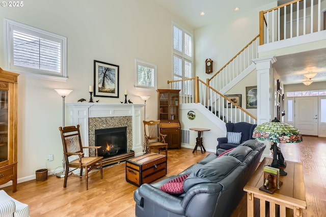 living room with a towering ceiling, light wood-style floors, a glass covered fireplace, stairs, and recessed lighting
