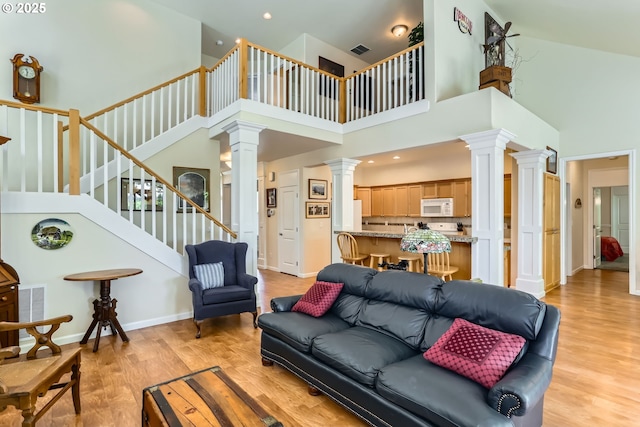 living area featuring decorative columns, a high ceiling, light wood-type flooring, stairs, and baseboards