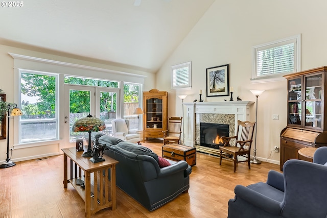 living area with high vaulted ceiling, a fireplace, light wood-type flooring, and baseboards