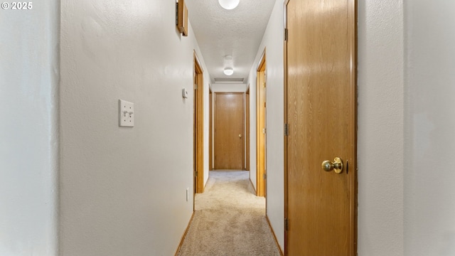 hall featuring light colored carpet and a textured ceiling