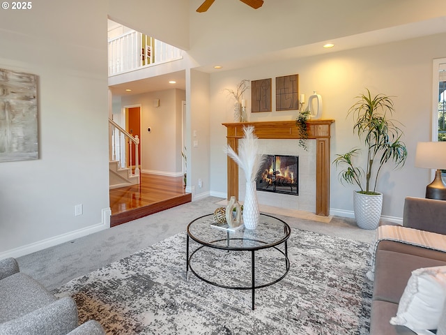 living room featuring ceiling fan, a tiled fireplace, carpet, and a high ceiling